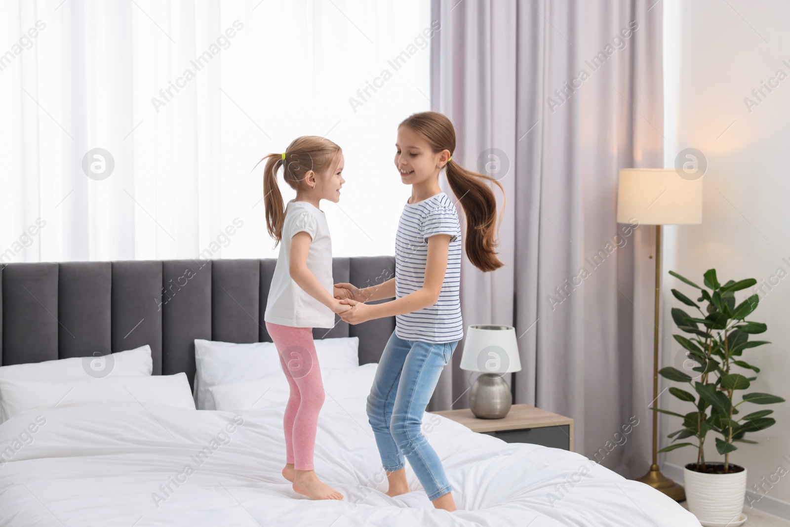 Photo of Cute little sisters having fun together on bed at home