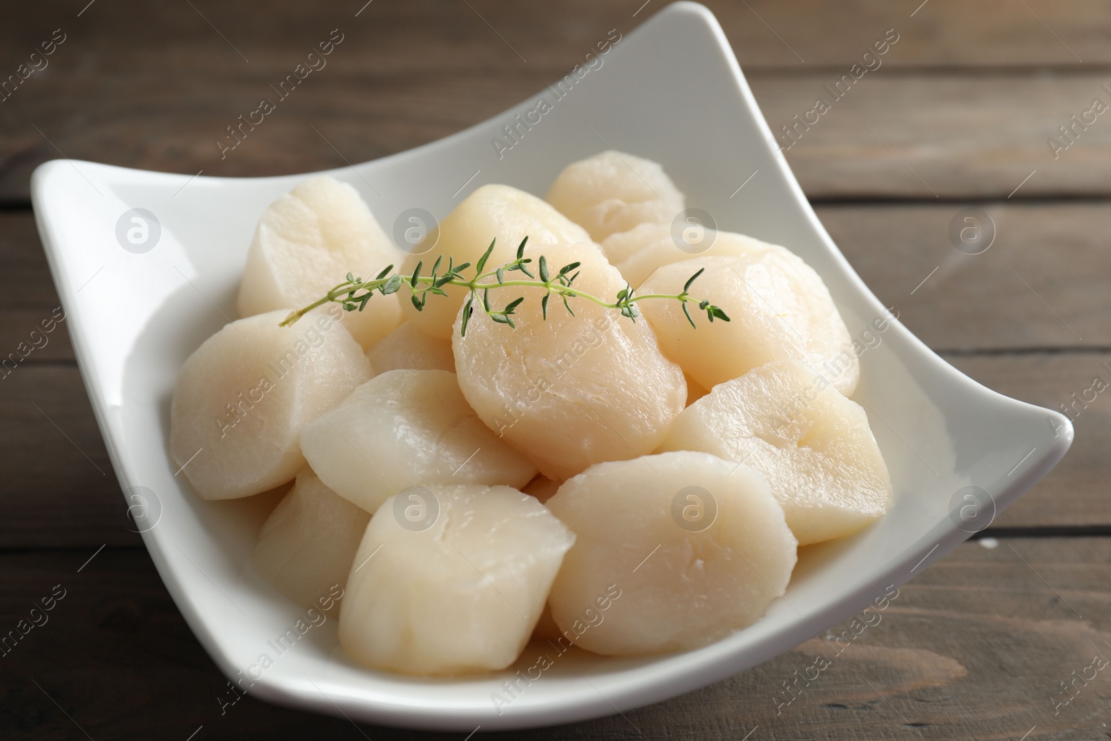 Photo of Fresh raw scallops and thyme in bowl on wooden table, closeup