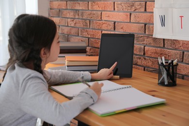 Little girl doing homework with modern tablet at home, focus on hand