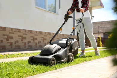 Photo of Woman cutting green grass with lawn mower on backyard, closeup