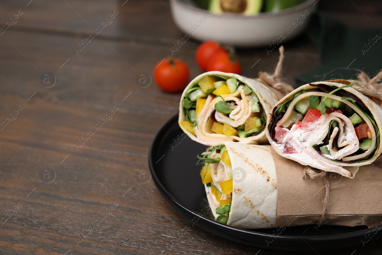 Photo of Delicious sandwich wraps with fresh vegetables on wooden table, space for text