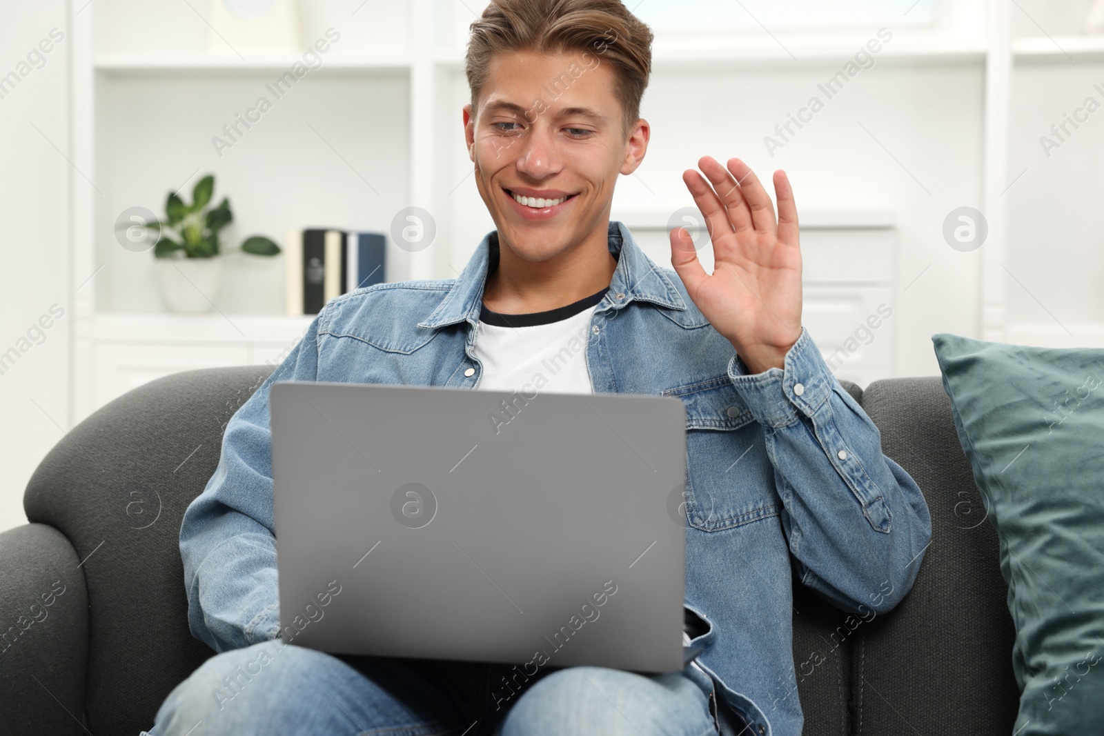 Photo of Happy young man having video chat via laptop on sofa indoors