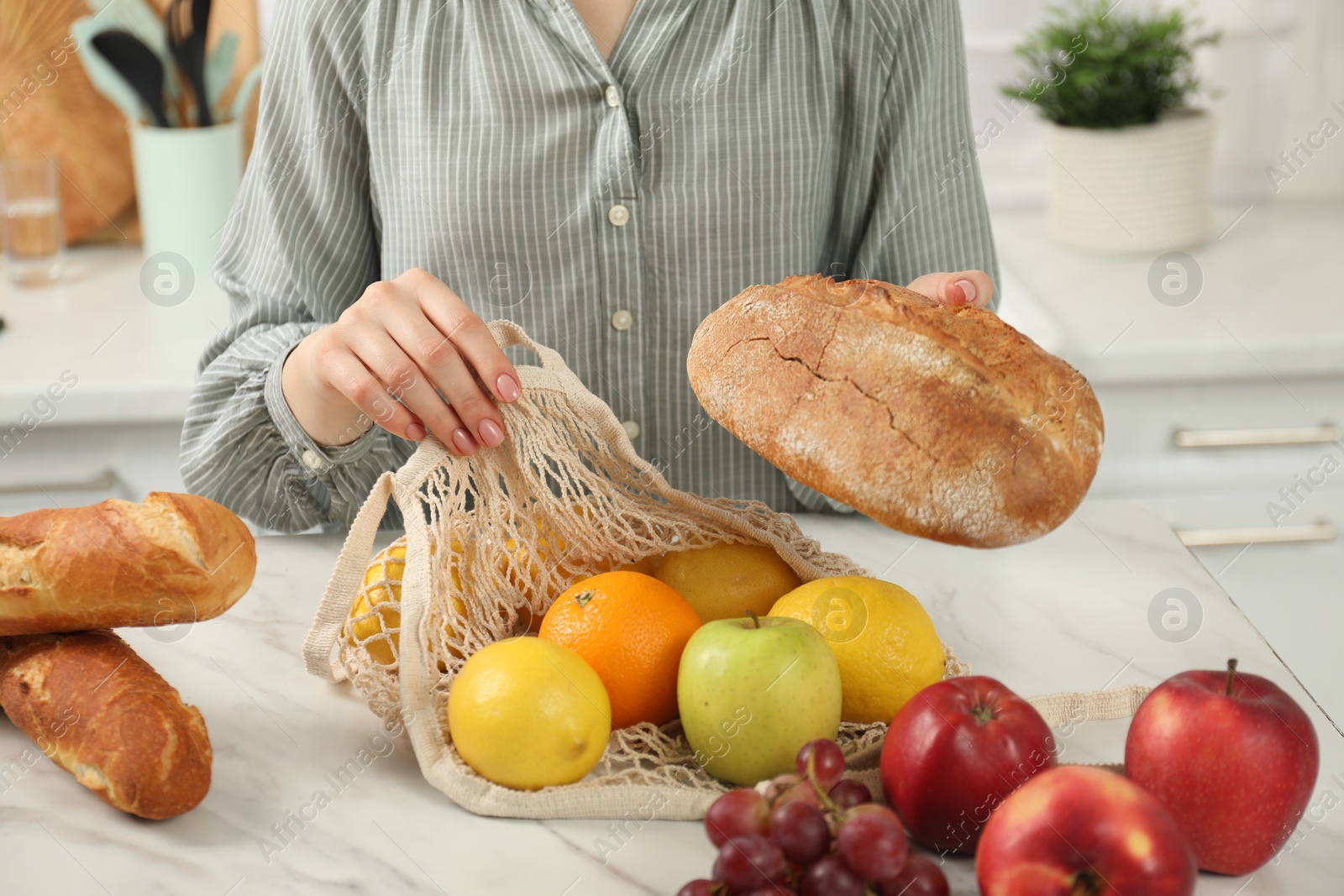 Photo of Woman with string bag of fresh fruits and bread at light marble table, closeup