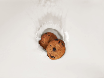 Photo of Cookies falling in milk with splashes, top view