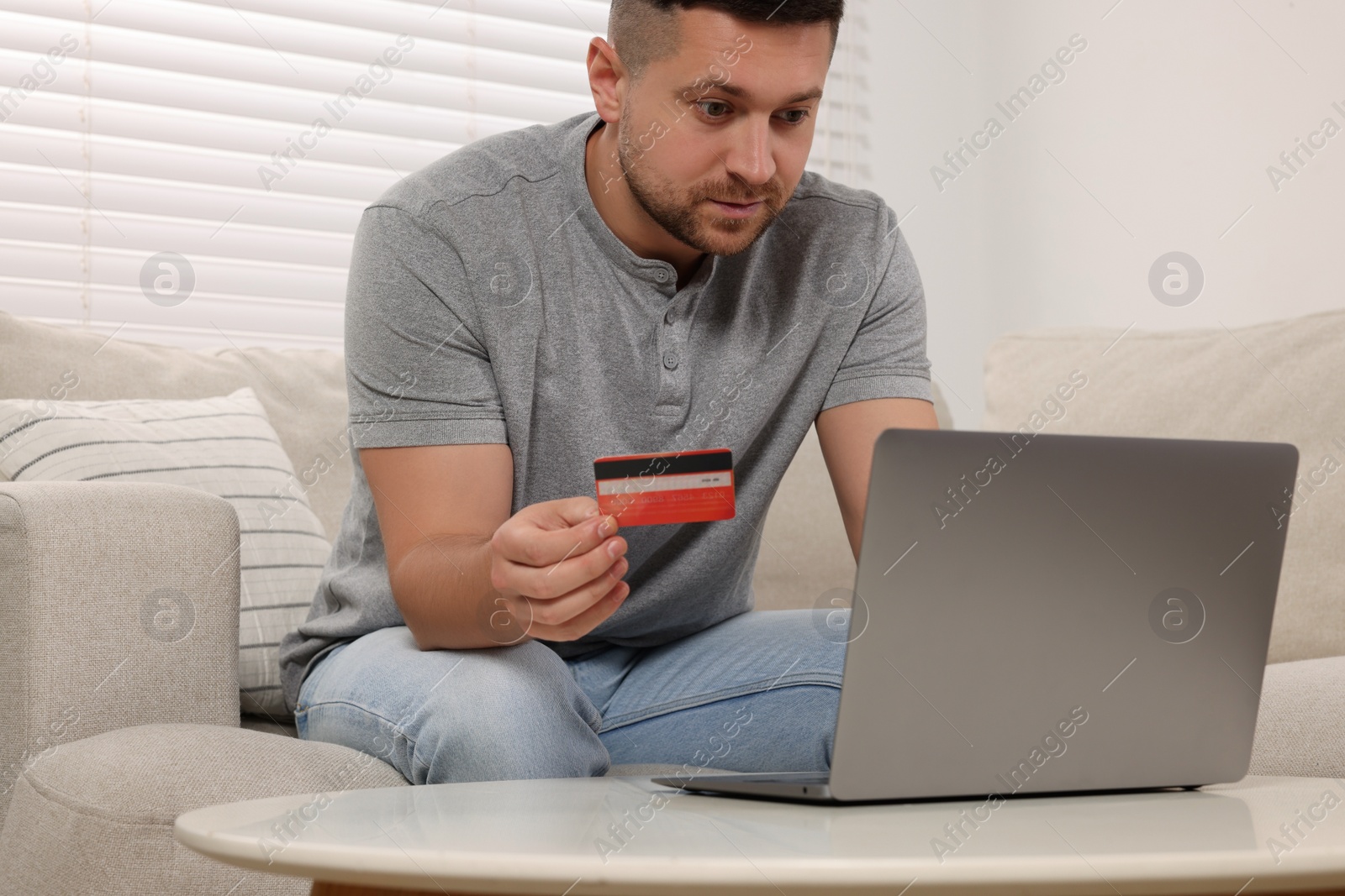 Photo of Handsome man with credit card using laptop for online shopping at home