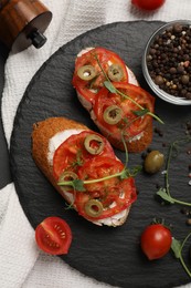 Delicious ricotta bruschettas with sliced tomatoes, olives and greens on black table, top view