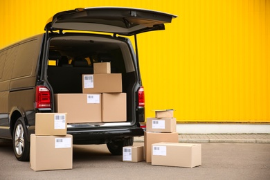 Photo of Black delivery van and many different parcels near yellow wall outdoors, space for text. Courier service