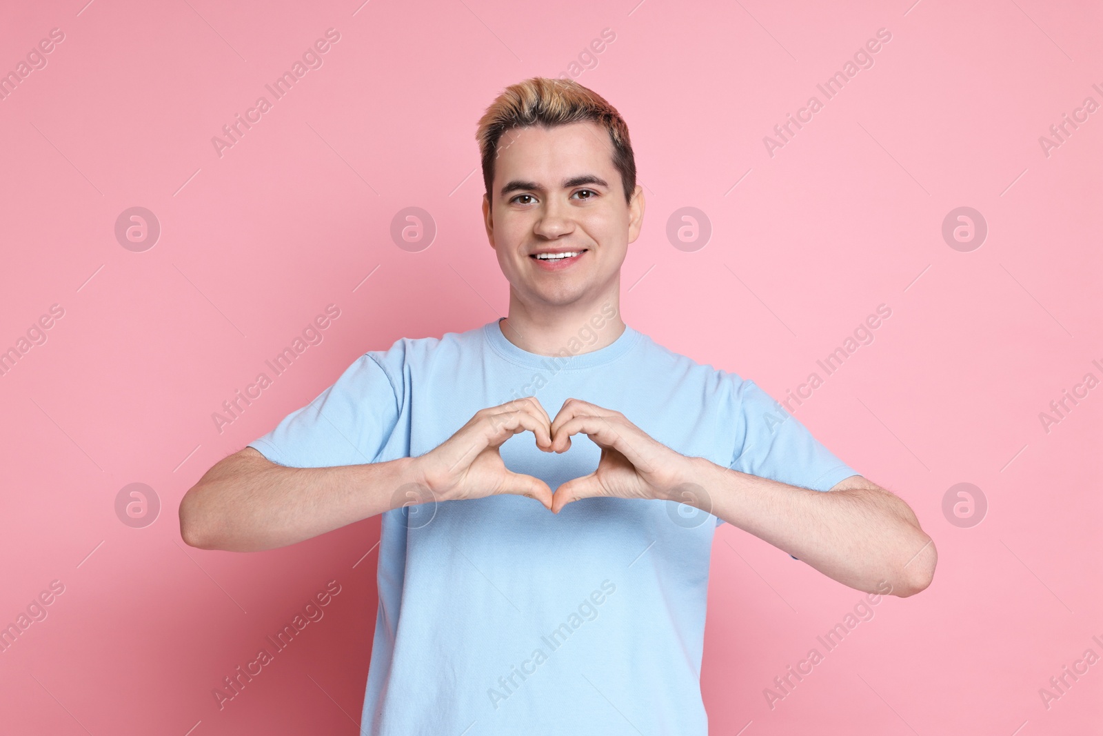 Photo of Young man showing heart gesture with hands on pink background