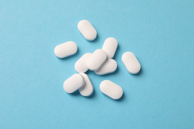 Pile of white pills on light blue background, flat lay