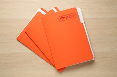 Image of Top Secret stamp. Orange files with documents on wooden table, top view