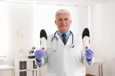 Photo of Senior male orthopedist showing insoles in clinic