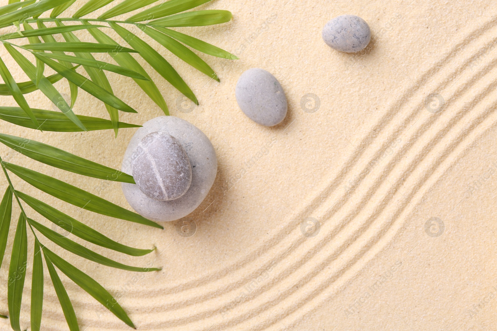 Photo of Zen garden stones and green leaves on sand with pattern, flat lay. Space for text