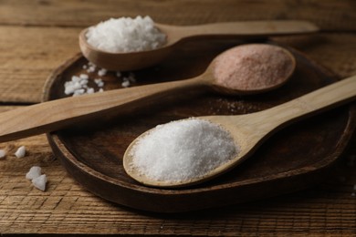 Photo of Different natural salt in spoons on wooden table, closeup