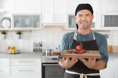 Photo of Professional male chef holding board with meat in kitchen