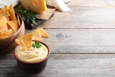 Delicious cheese sauce with nacho and parsley on wooden table, space for text