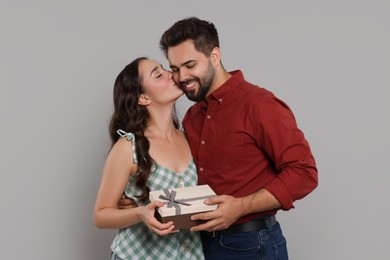 Photo of Woman kissing her smiling boyfriend on grey background. Celebrating holiday
