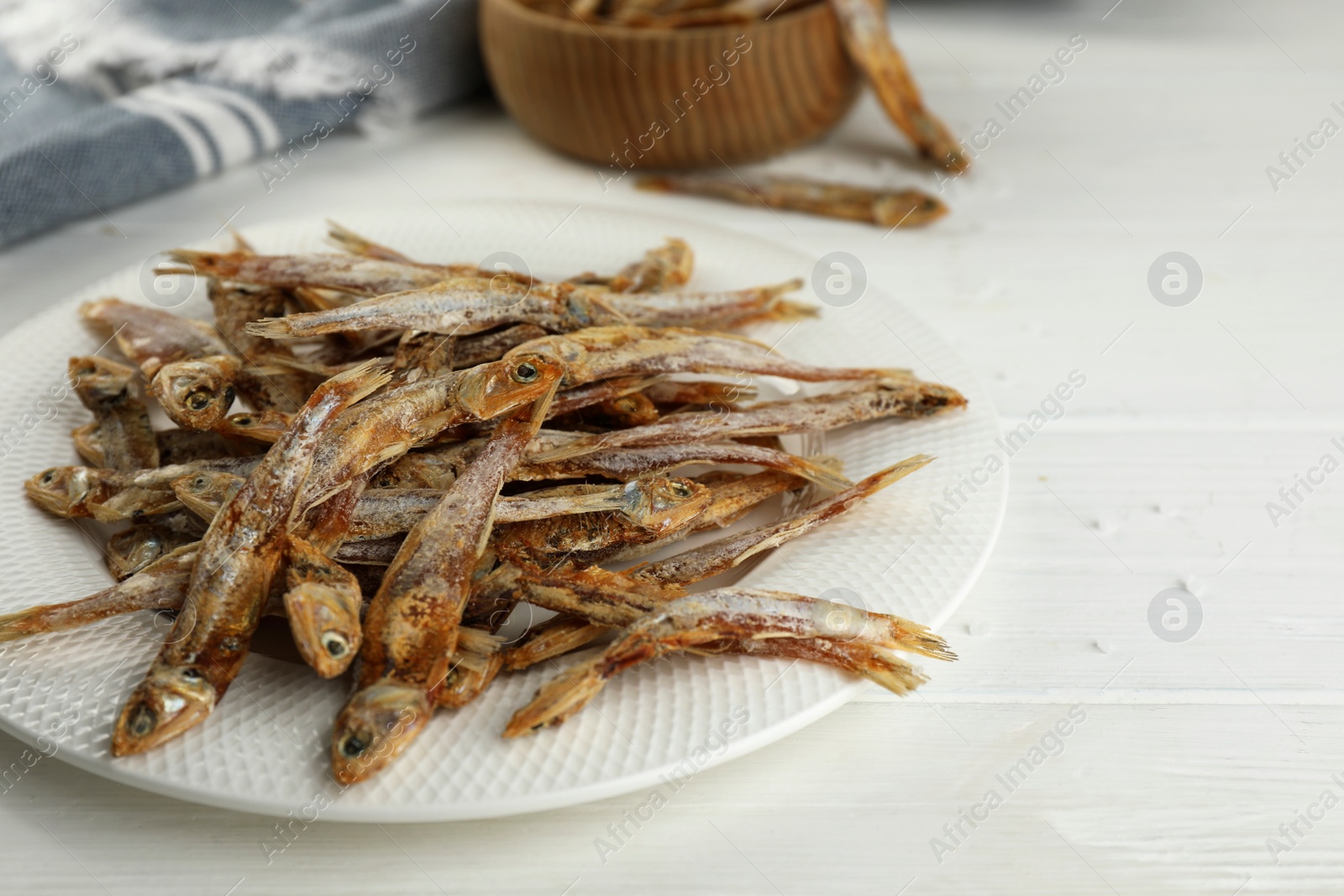 Photo of Plate with tasty dried anchovies on white wooden table, closeup