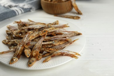 Plate with tasty dried anchovies on white wooden table, closeup