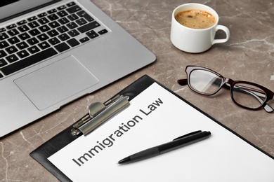 Photo of Clipboard with words IMMIGRATION LAW and laptop on table, closeup