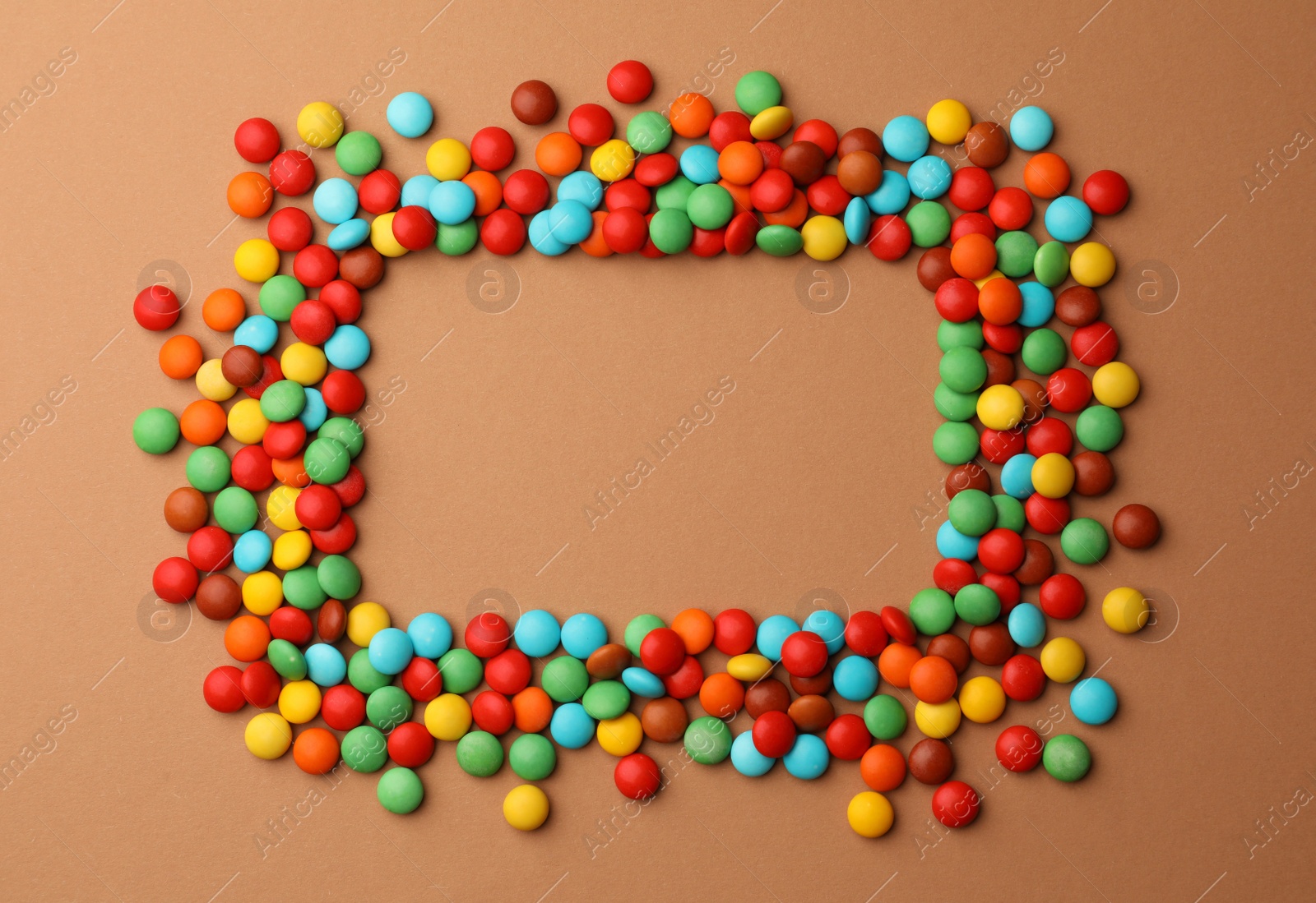 Photo of Frame of tasty colorful candies on light brown background, flat lay. Space for text