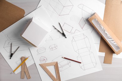 Creating packaging design. Drawings, boxes and stationery on light wooden table, flat lay