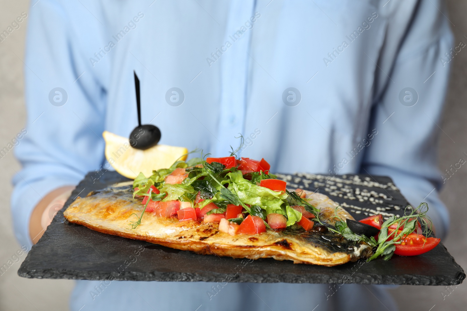 Photo of Woman holding slate plate with delicious grilled fish, closeup