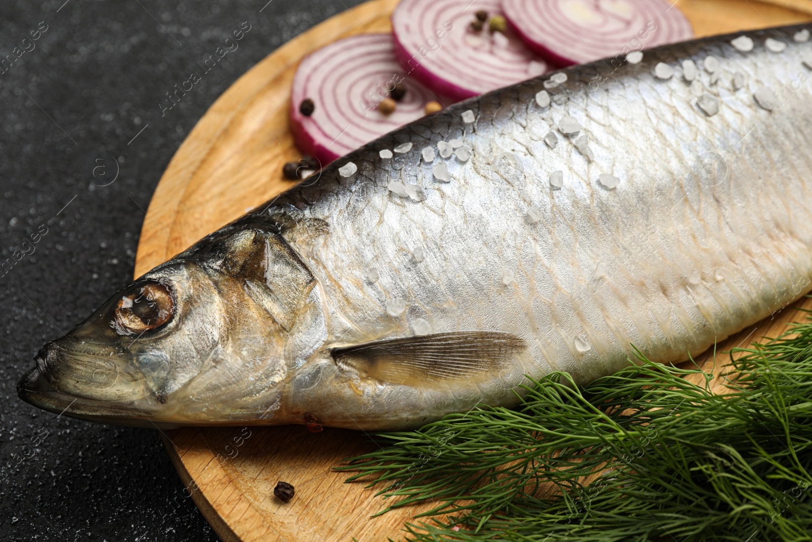 Photo of Delicious salted herring, dill and onion on dark grey table, closeup