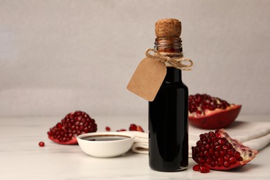Photo of Glass bottle of pomegranate sauce and fresh ripe fruit on white marble table. Space for text