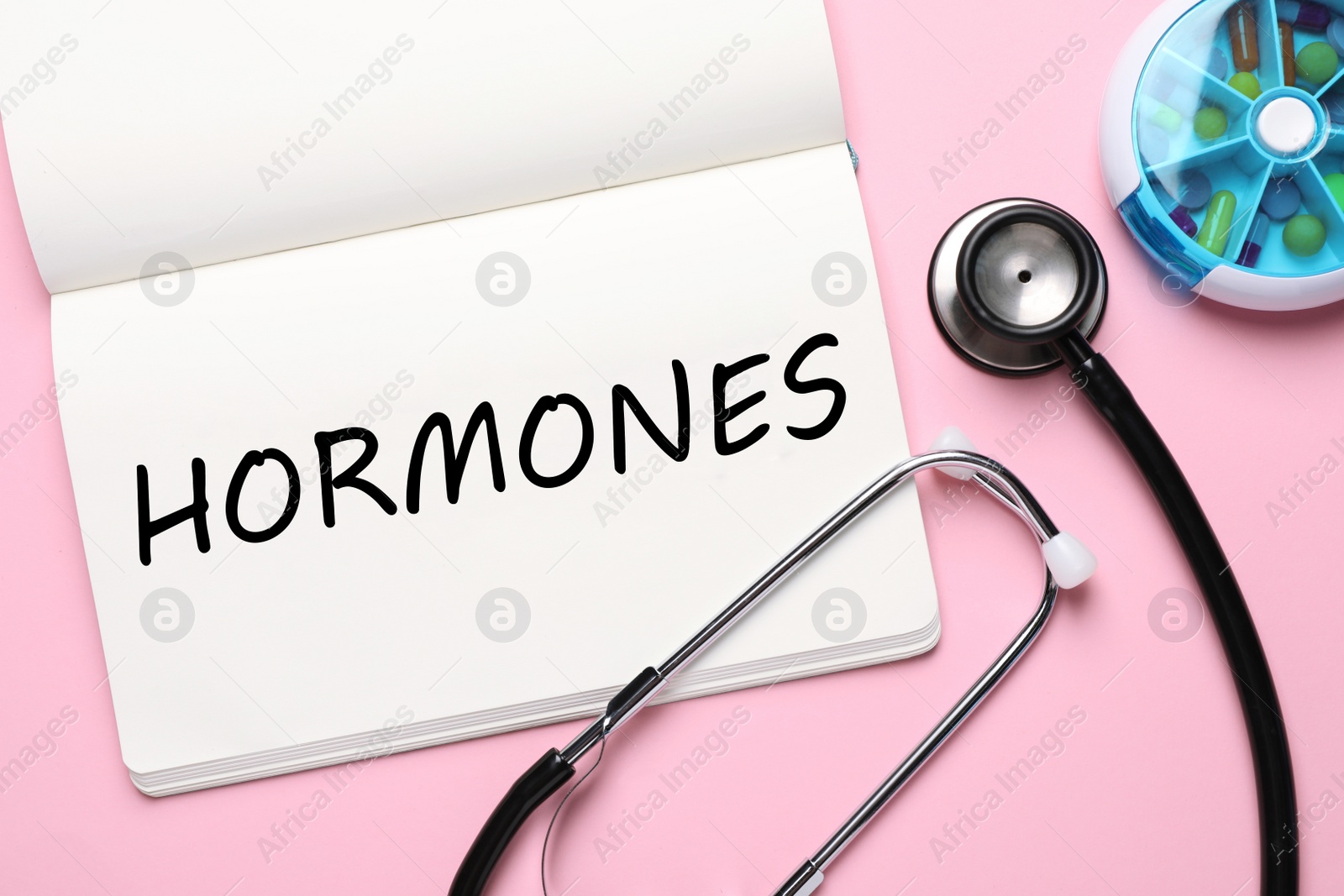 Photo of Notebook with word Hormones, stethoscope and pills on pink background, flat lay