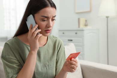 Confused woman with credit card talking on phone at home. Be careful - fraud