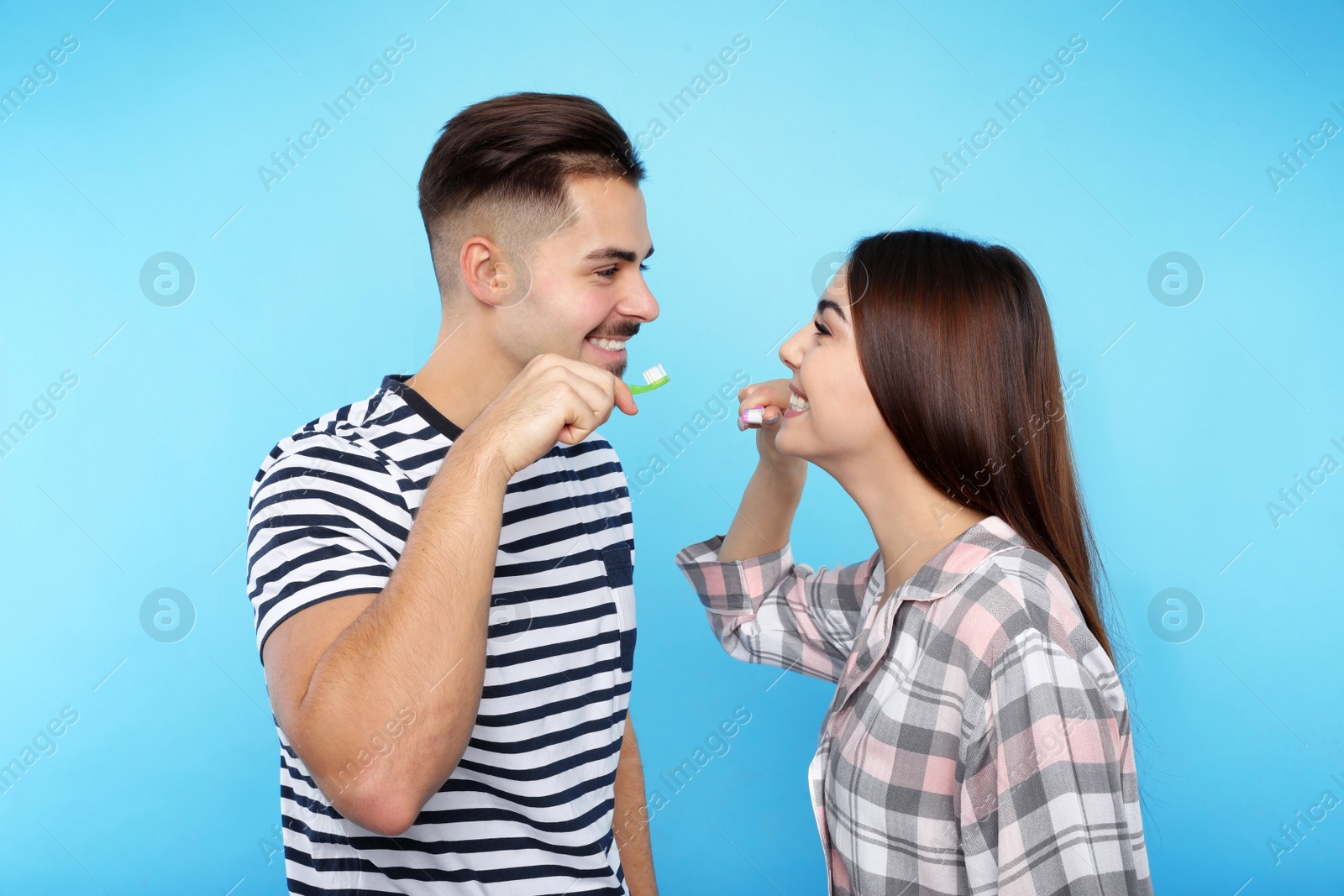 Photo of Happy couple brushing teeth on color background