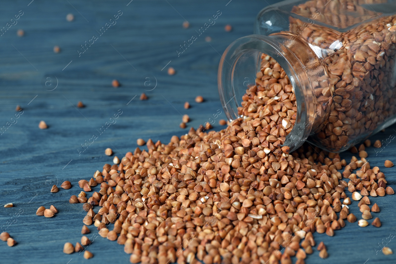 Photo of Overturned glass jar with uncooked buckwheat on table