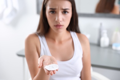 Young woman holding cotton pad with fallen eyelashes indoors