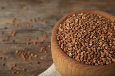 Uncooked buckwheat in bowl on wooden table, closeup. Space for text