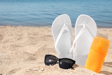 Stylish flip flops, sunglasses and sun protection spray on sandy beach, space for text