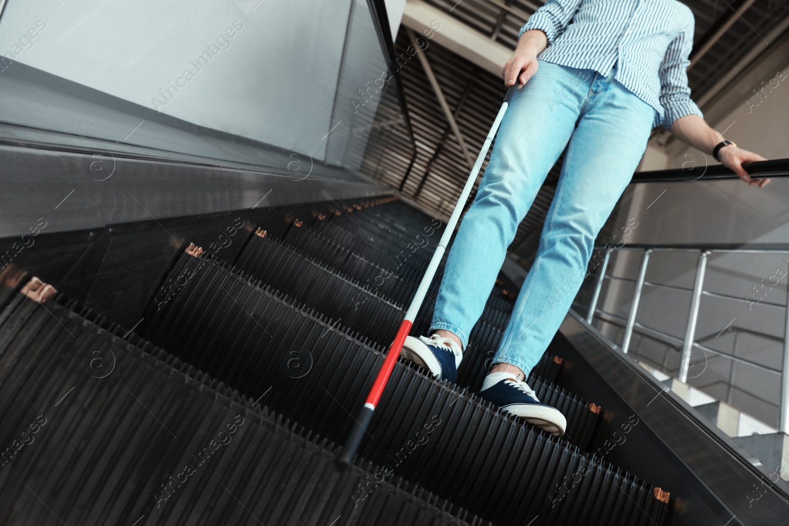 Photo of Blind person with long cane on escalator indoors