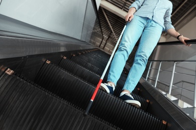 Blind person with long cane on escalator indoors