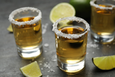 Photo of Mexican Tequila shots, lime slices and salt on grey table