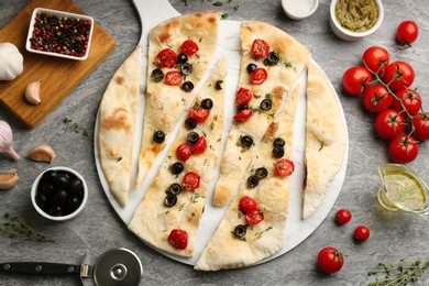Delicious focaccia bread with olives and tomatoes on grey table, flat lay