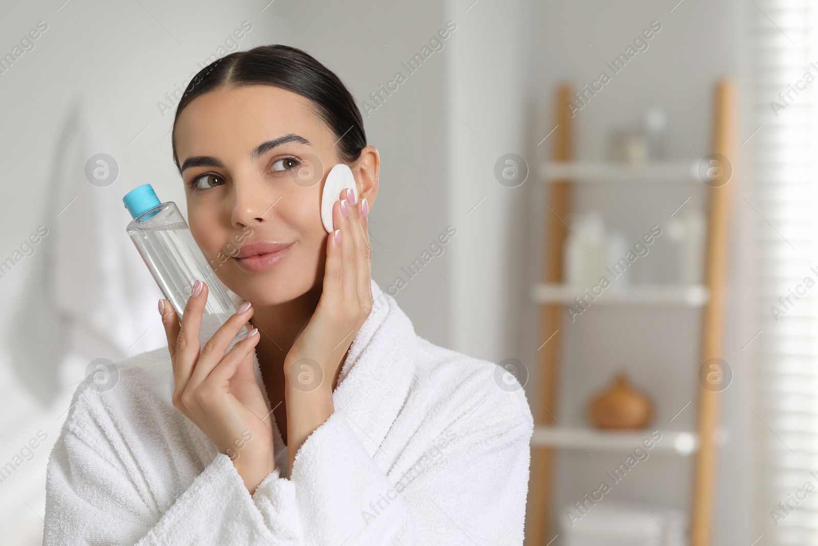 Photo of Beautiful woman removing makeup with cotton pad in bathroom, space for text