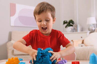 Cute little boy playing with bright kinetic sand at table in room