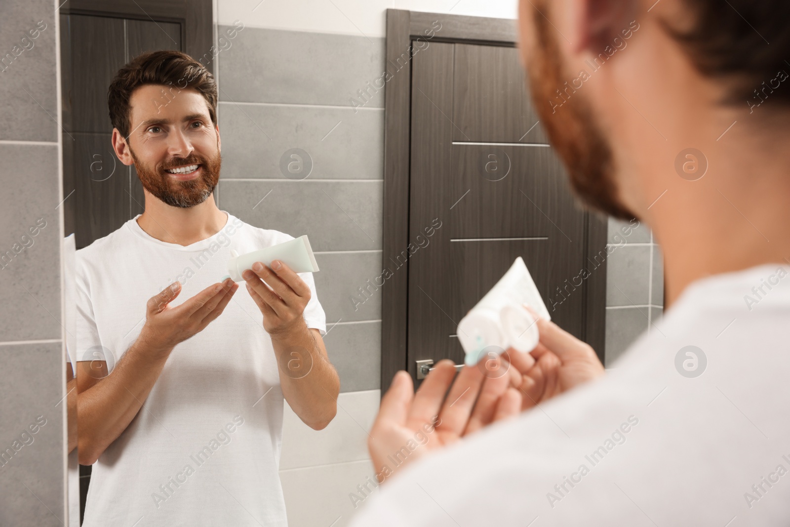 Photo of Handsome man applying cream on hand in bathroom