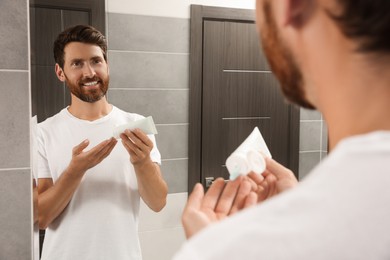 Photo of Handsome man applying cream on hand in bathroom