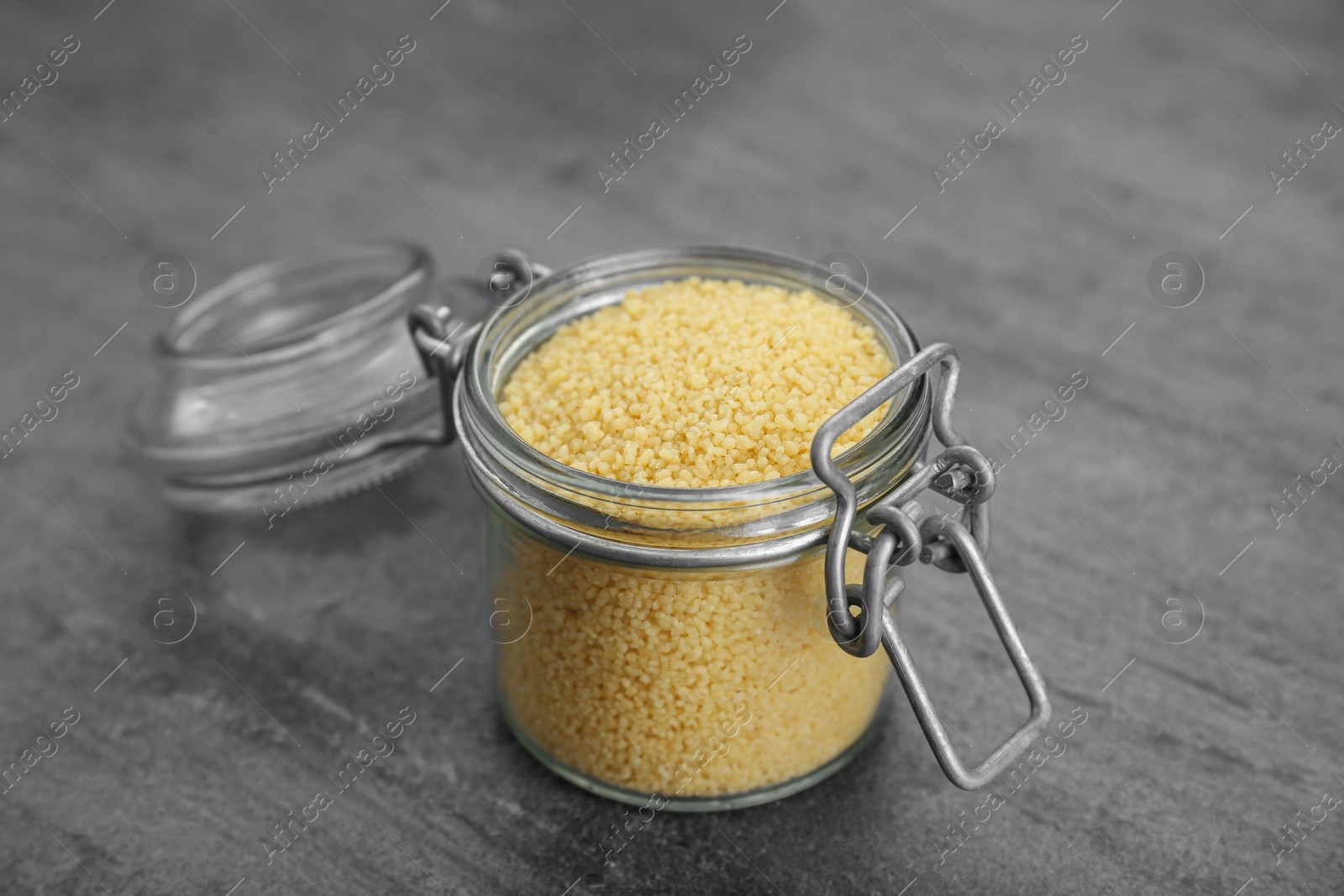 Photo of Glass jar of raw couscous on grey table, closeup
