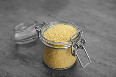Photo of Glass jar of raw couscous on grey table, closeup