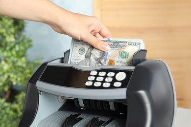 Photo of Woman putting money into counting machine indoors, closeup