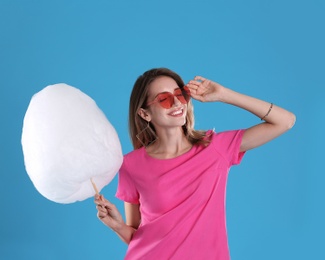 Photo of Happy young woman with cotton candy on blue background