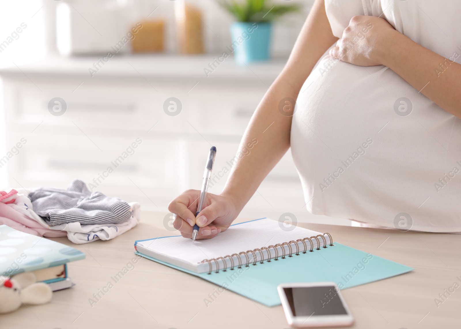 Photo of Pregnant woman writing packing list for maternity hospital in kitchen, closeup