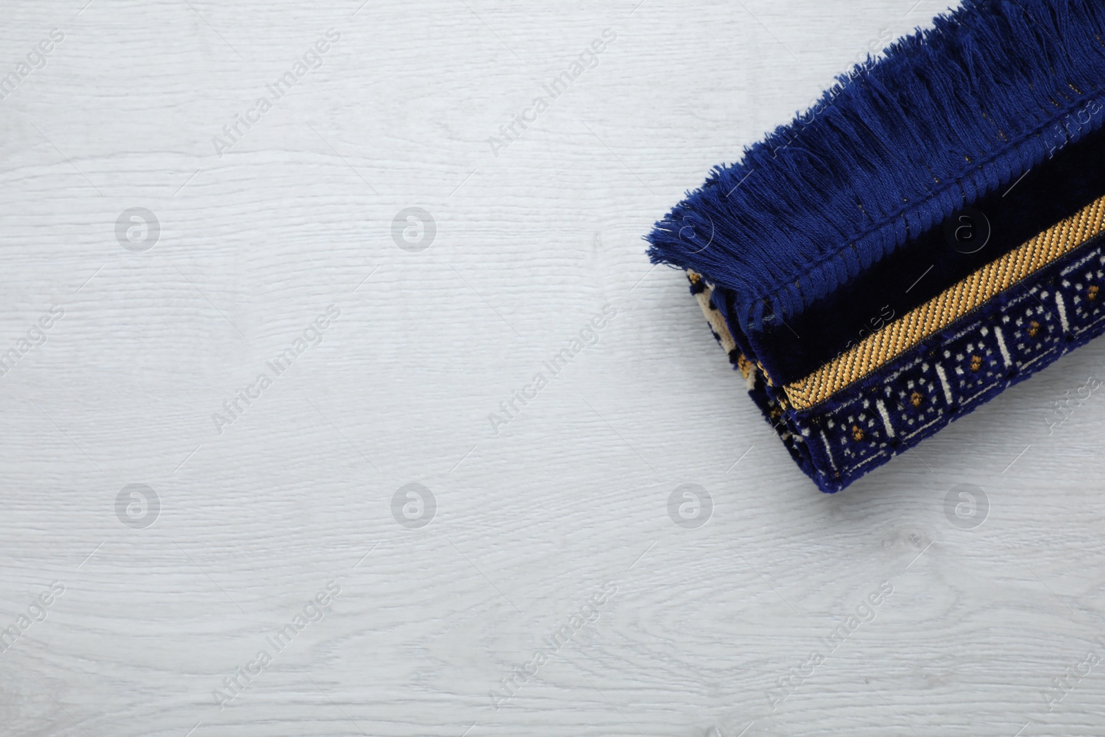 Photo of Muslim prayer rug on wooden floor, top view. Space for text