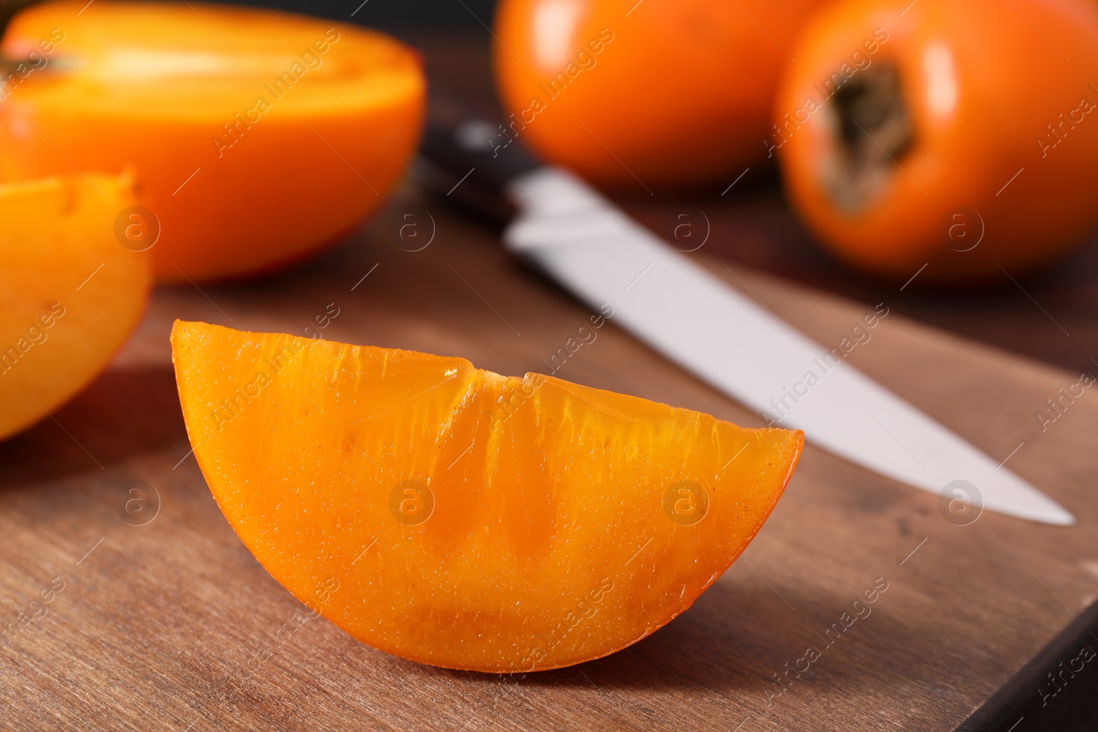 Photo of Piece of delicious ripe persimmon on wooden board, closeup